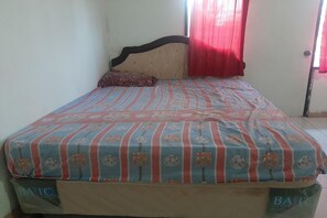 A bed with a striped bedspread, a headboard, a pillow, and a window with red curtains. - Spot ON 90535 Cimanuk Pavilion (Bengkulu)