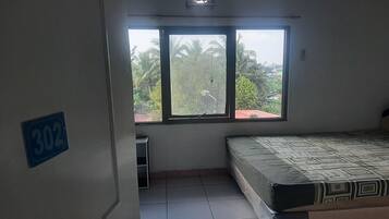 Une chambre avec un lit, une fenêtre donnant sur des palmiers et une porte avec un numéro.