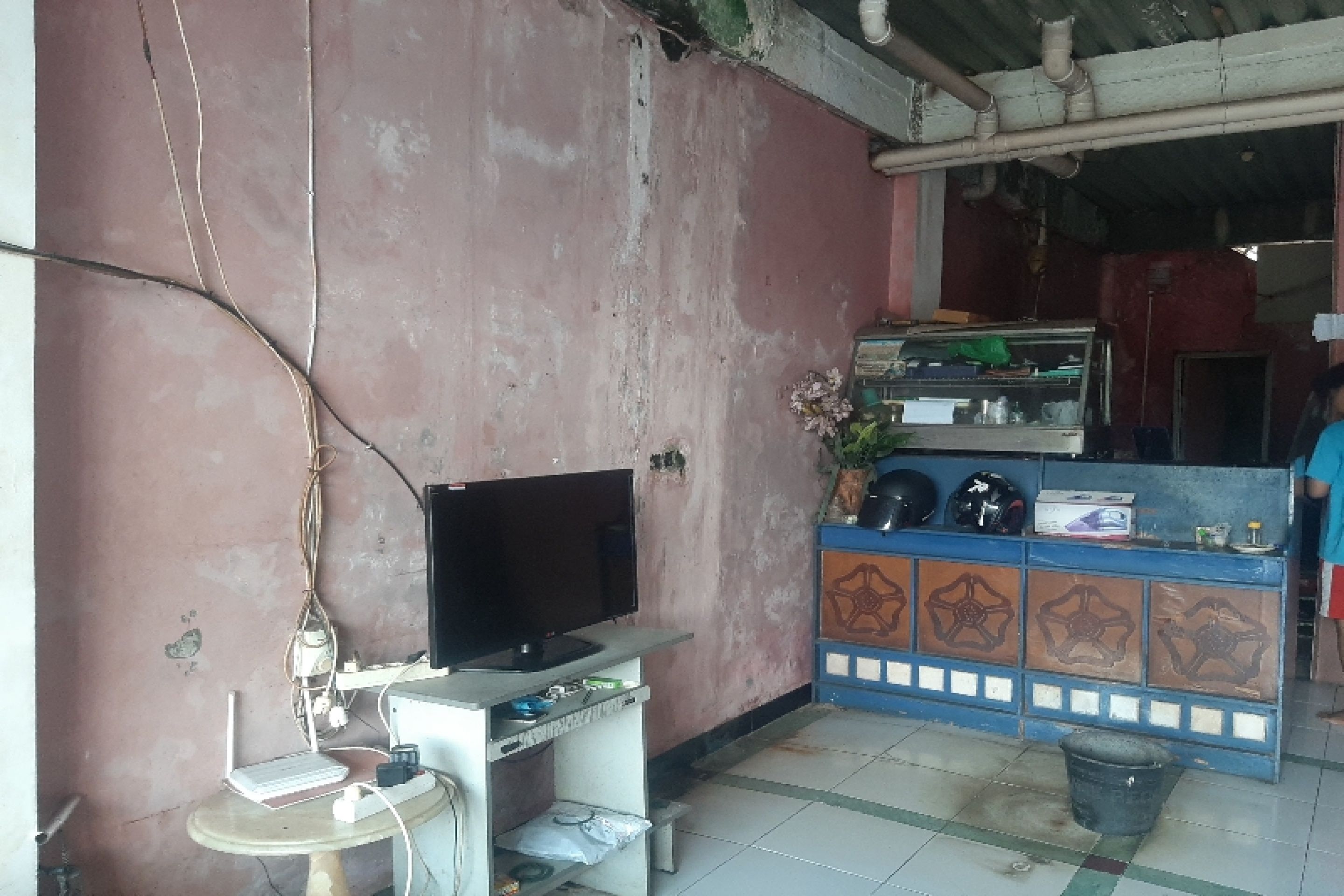 A room with a television on a stand, a small table with a laptop, and a decorative cabinet with items on top.