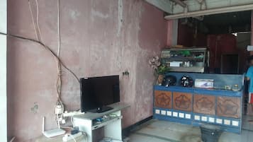 A room with a television on a stand, a small table with a laptop, and a decorative cabinet with items on top.