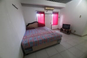 Une chambre à coucher avec un lit, un téléviseur posé sur un meuble et une porte avec des rideaux.