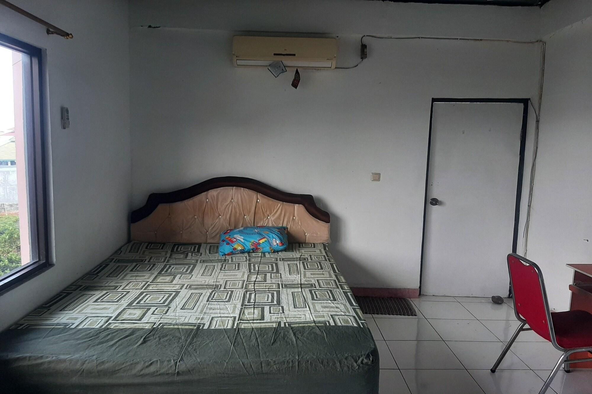 Ein Schlafzimmer mit einem gemusterten Bett, einem Holz-Kopfteil, einem Fenster, einer Tür und einem roten Sessel.