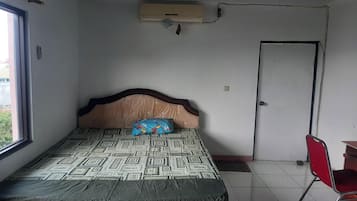 Ein Schlafzimmer mit einem gemusterten Bett, einem Holz-Kopfteil, einem Fenster, einer Tür und einem roten Sessel.