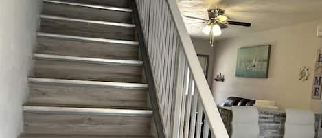 A wooden staircase with white railings leading to a landing area with a ceiling fan and a painting.
