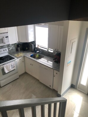 A kitchen with white cabinets, a granite countertop, a stainless steel sink, a microwave, and a stove. - Cute renovated 2 bedroom condo just minutes from Sanibel (Fort Myers)