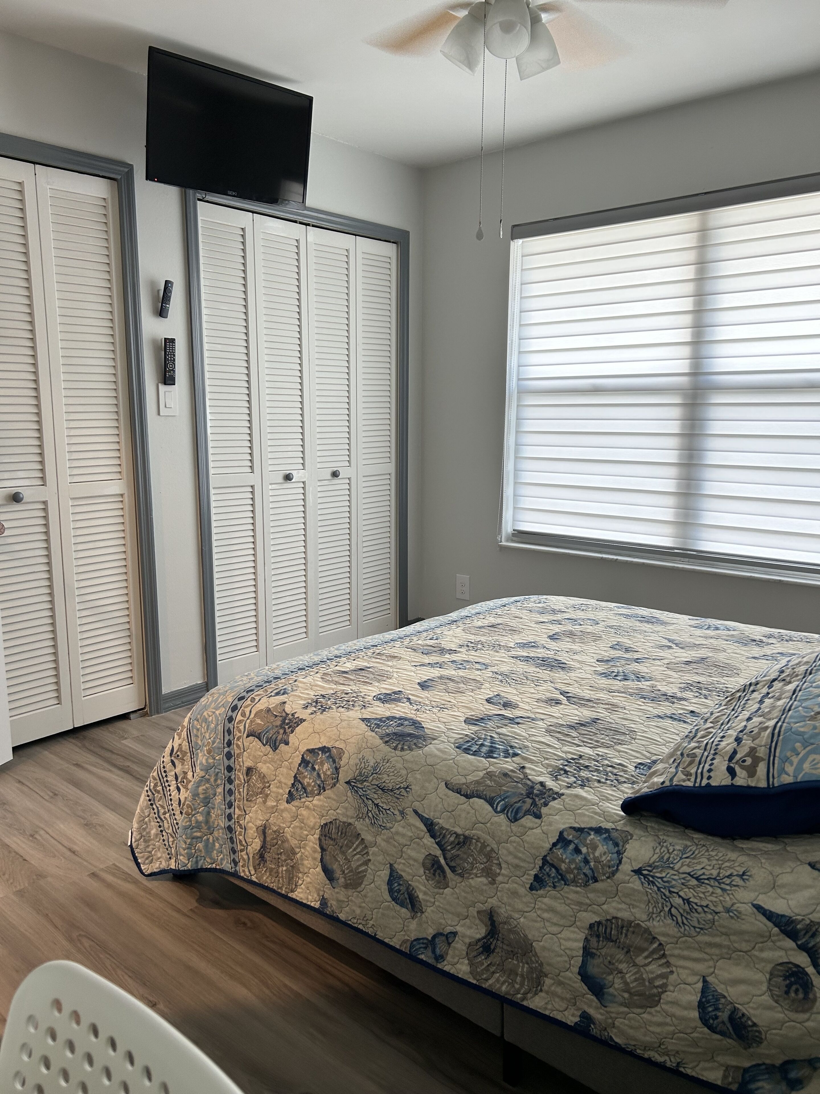 A bedroom with a bed, a ceiling fan, a window with blinds, and a wardrobe.
