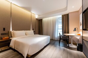 A hotel room with a large bed, a desk, a chair, and a view of the city through the window.