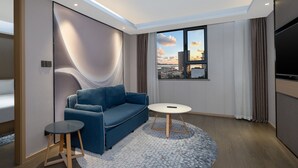 A modern living room with a blue sofa, a small round table, and a view of the cityscape through a large window.