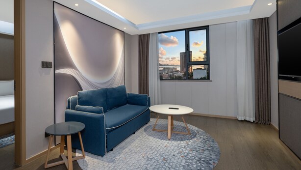Una sala de estar moderna con un sofá azul, una mesita redonda y vistas a la ciudad a través de un ventanal grande.
