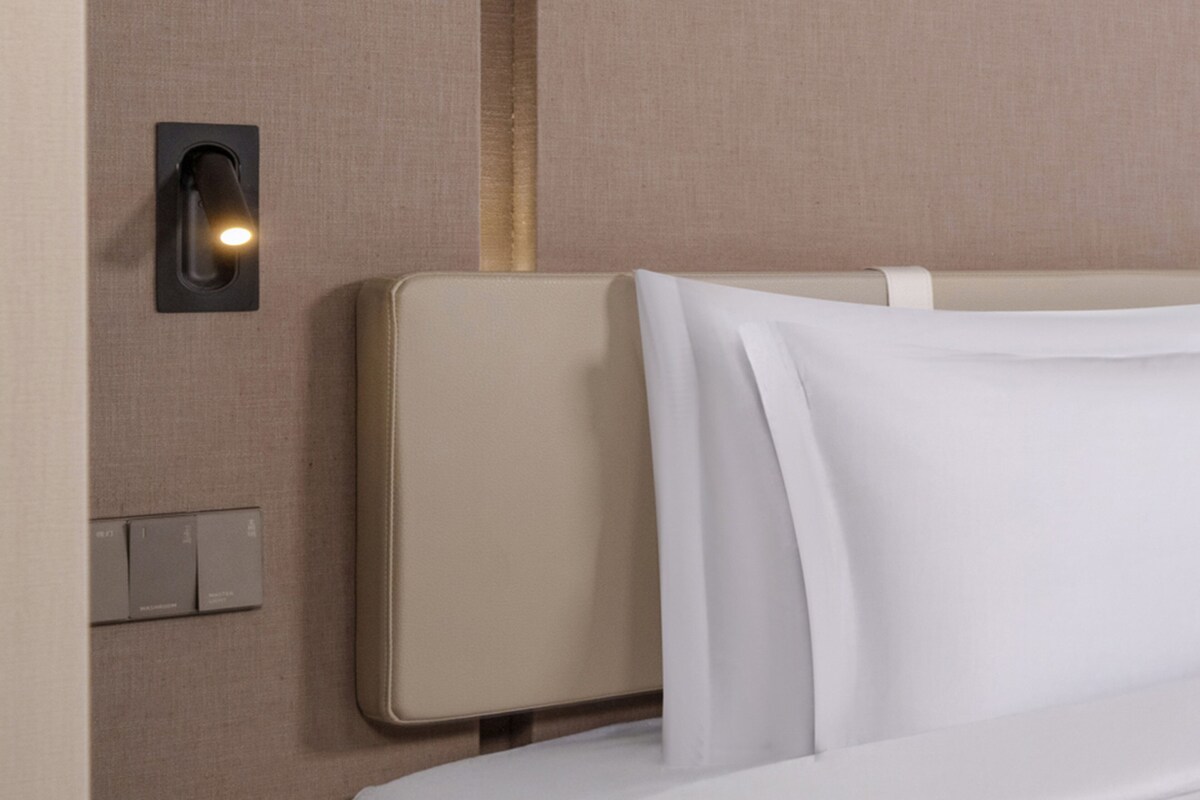 Una habitación de hotel con una cama, una lámpara en la pared y un panel de control.