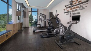 Un gimnasio moderno con máquinas de cardio, una pared con frases motivacionales y vistas a zonas verdes exteriores.