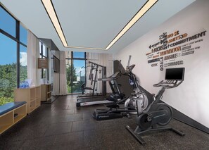 Un gimnasio moderno con máquinas de cardio, una pared con frases motivacionales y vistas a zonas verdes exteriores.