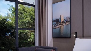 Una habitación de hotel moderna con un ventanal grande, una cama, un sofá y un cuadro de un puente.
