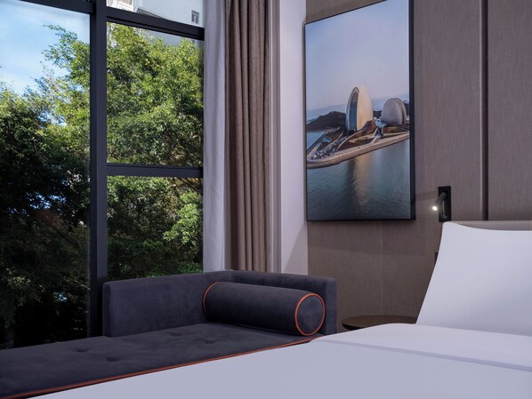 Una habitación de hotel moderna con un ventanal grande, una cama, un sofá y un cuadro de un puente.