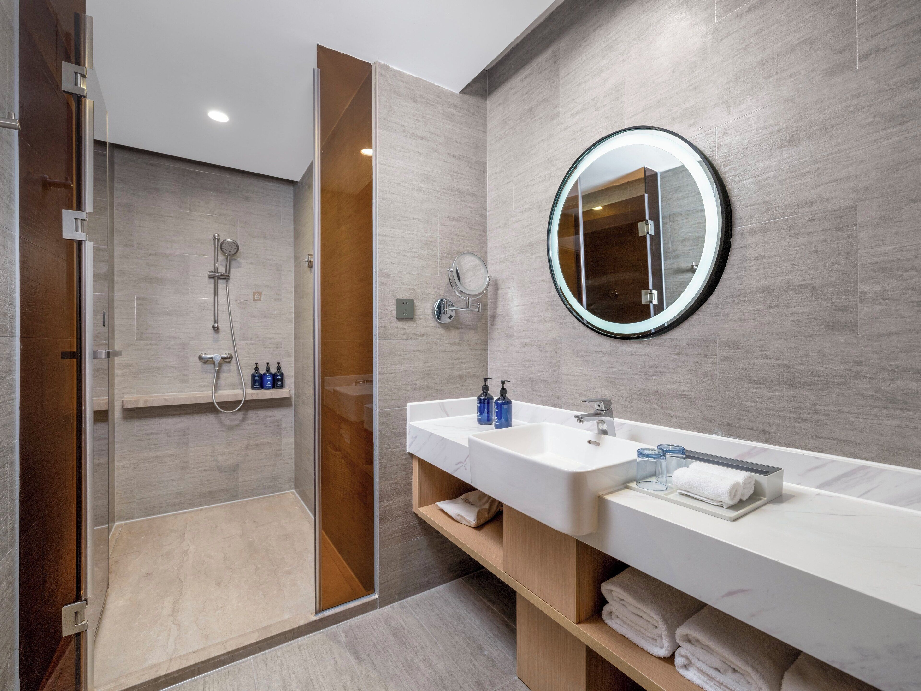 A modern bathroom with a glass-enclosed shower, a large mirror, and a white vanity with a marble countertop.