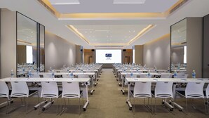 Un salón de conferencias con varias mesas y sillas, equipado con botellas de agua y pantallas de presentación.