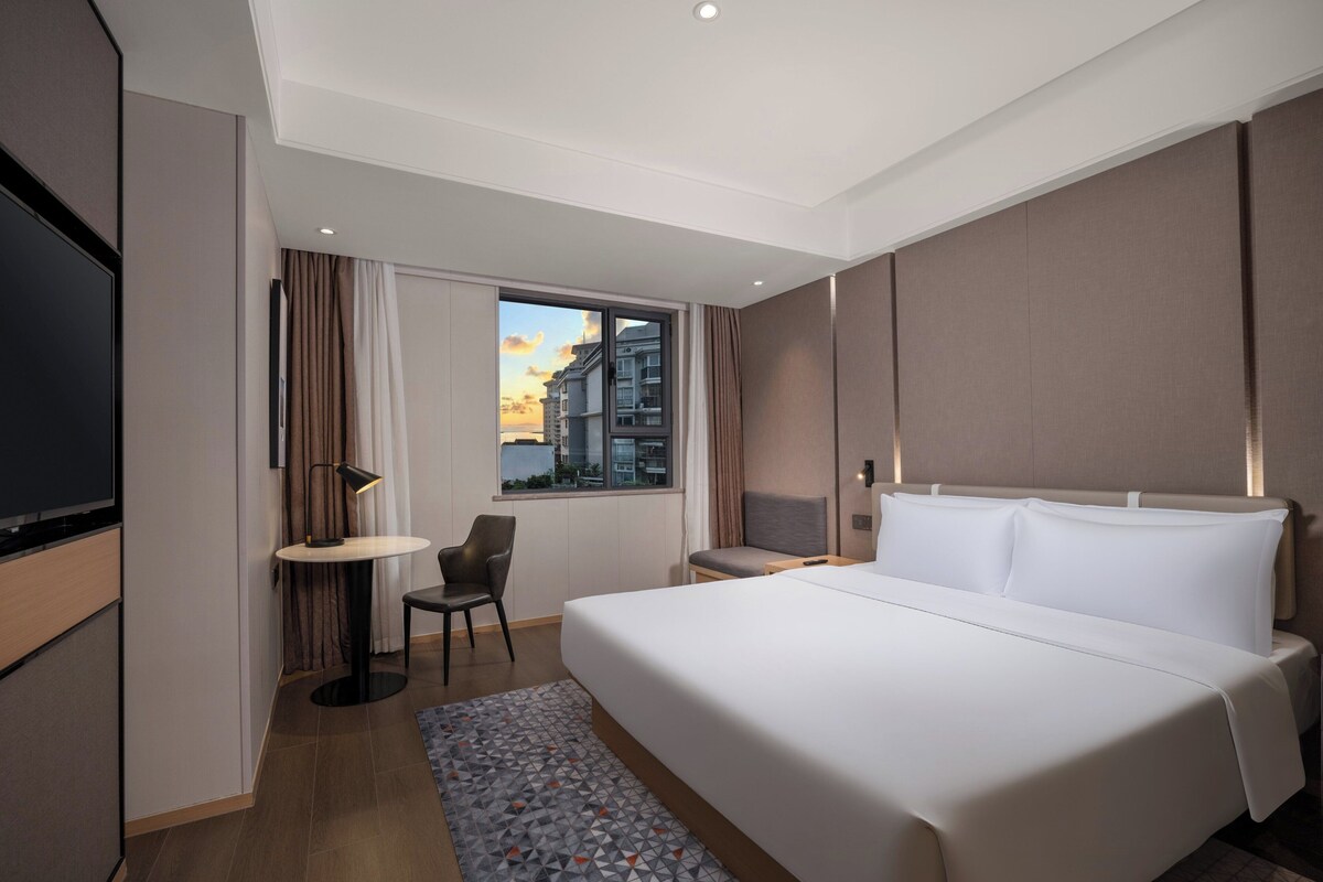 Una habitación de hotel moderna con una cama grande, un escritorio, una silla y un televisor.