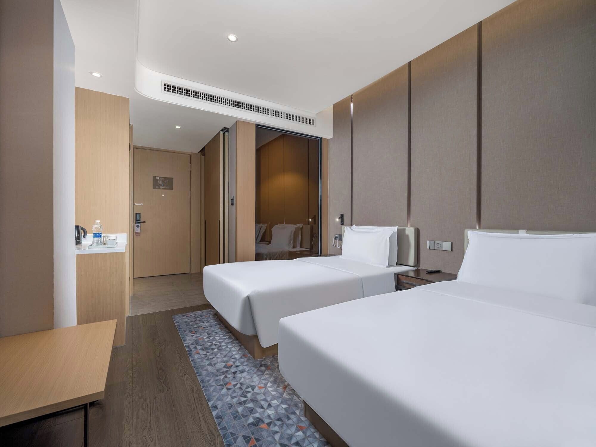 A hotel room with two beds, a small table, a coffee machine, and a bathroom visible through an open door.