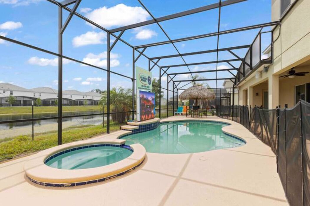 A pool area with a hot tub, a covered seating area, and a view of a water body and distant buildings.