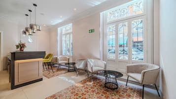 Un hall d’hôtel comprenant un comptoir d’accueil, un espace salon, un tapis à motifs et de grandes fenêtres agrémentées d’éléments décoratifs en fer forgé.