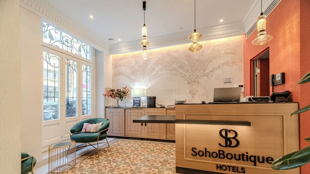 A reception area with a wooden desk, a green chair, and a patterned floor. - Soho Boutique Turia (Valencia)