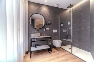 Un baño moderno con un espejo grande, un lavabo, un inodoro y una ducha con mampara de vidrio.