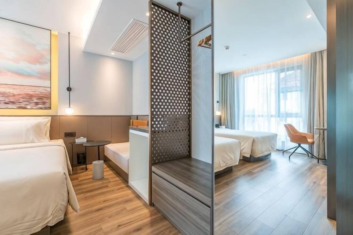 A hotel room with two beds, a desk, a chair, a small table, and a decorative screen.