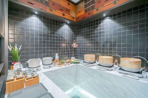 A modern kitchen with black tiled walls, a central island, and various cooking utensils and appliances. - Shanghai Baoshan Changjiang Road Atour Light Residence Hotel (Shanghai)