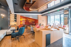 A modern hotel lobby with a reception desk, seating area, and a large window providing a view of the outdoors.