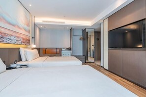 A modern hotel room with a large bed, a TV, and a small kitchenette.