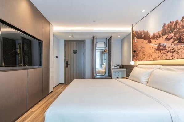 A modern hotel room with a large bed, a wardrobe, a mirror, and a painting on the wall.
