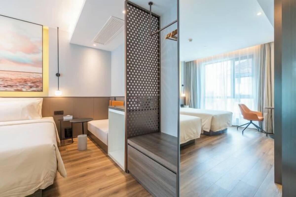 A hotel room with two beds, a small table, a chair, and a large window.