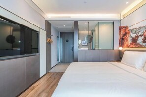 A modern hotel room with a large bed, a walk-in closet, a bathroom with a glass shower, and a dining area with a view.