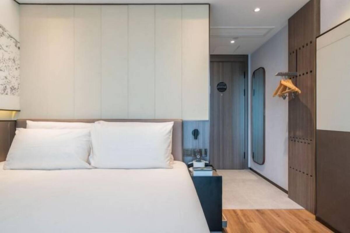 A modern hotel room with a large bed, a wardrobe, a mirror, and a door leading to another room.