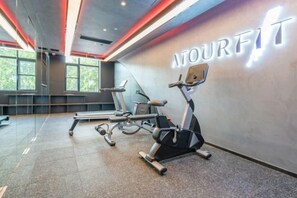 Un gimnasio con cintas de correr y bicicletas estáticas, una pared con la palabra 'MOURFIT' iluminada y un ventanal grande que proporciona luz natural.