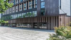 Un bâtiment moderne doté d’une façade en verre, une enseigne indiquant « ATOURLIGHT », et un espace de stationnement avec des voitures.