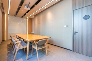 Un salón de conferencias con una larga mesa, seis sillas, un proyector y una puerta con un cartel.