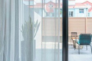 A view through a window with sheer curtains, revealing a patio area with outdoor furniture and a wooden fence. - Shanghai Baoshan Changjiang Road Atour Light Residence Hotel (Shanghai)
