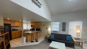 Una sala de estar moderna con un sofá, una mesa de centro y una cocina con taburetes de bar.