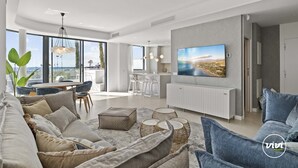 A modern living room with a large TV, comfortable seating, and a balcony with a view.