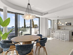 A modern kitchen with a central island, bar stools, and a dining area with round table and chairs. - Sunrise | Private Pool - Beachfront - Terrace (Torremolinos)