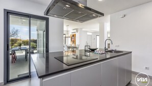 A modern kitchen with a large island, stainless steel appliances, and a sliding glass door leading to an outdoor area.