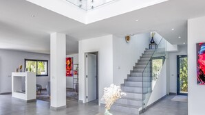 A spacious, modern interior with a central seating area, a staircase, and a glass railing on the upper level.