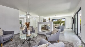 A modern living room with grey sofas, a glass coffee table, and a view of the outdoor seating area.