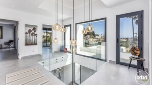 A modern interior with a glass staircase, pendant lighting, and a view of the city.