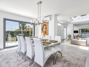 A modern dining area with a glass table, white chairs, and a large painting on the wall.