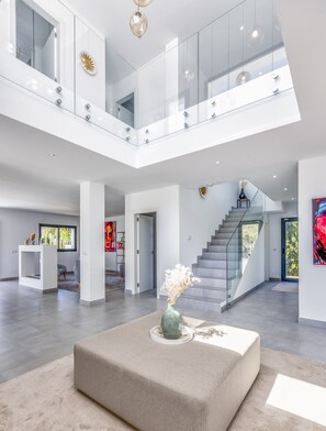A spacious, modern interior with a central seating area, a staircase, and a glass railing on the upper level. - Villa Ruby | Pool - terrace - views (Sitio de Calahonda)