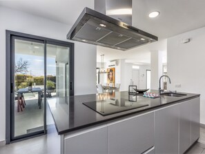 Une cuisine moderne dotée d’un grand îlot central, d’appareils électroménagers en acier inoxydable et d’une porte-fenêtre coulissante donnant sur un espace extérieur.
