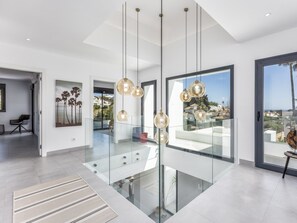 Un intérieur moderne avec un escalier en verre, des luminaires suspendus et une vue sur la ville.