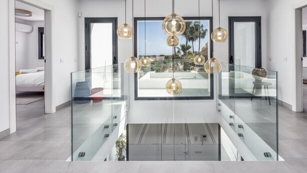 Ein modernes Interieur mit Glastrennwand, einem zentralen Chandelier und Blick ins Freie.